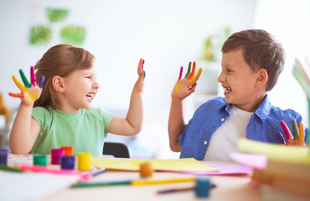 funny kids show their palms the painted paint. creative classes fine arts. two children a boy and a girl laugh. selective focusing on the palm. happy kids in drawing school
