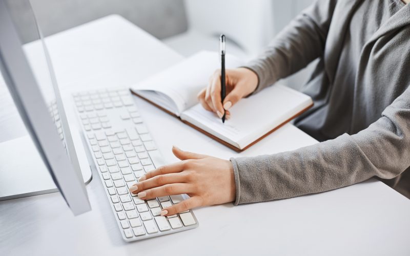 I can handle multi tasks. Cropped shot successful girl typing on keyboard and making notes while looking at computer screen and studying new business graphic. There is no time for rest.