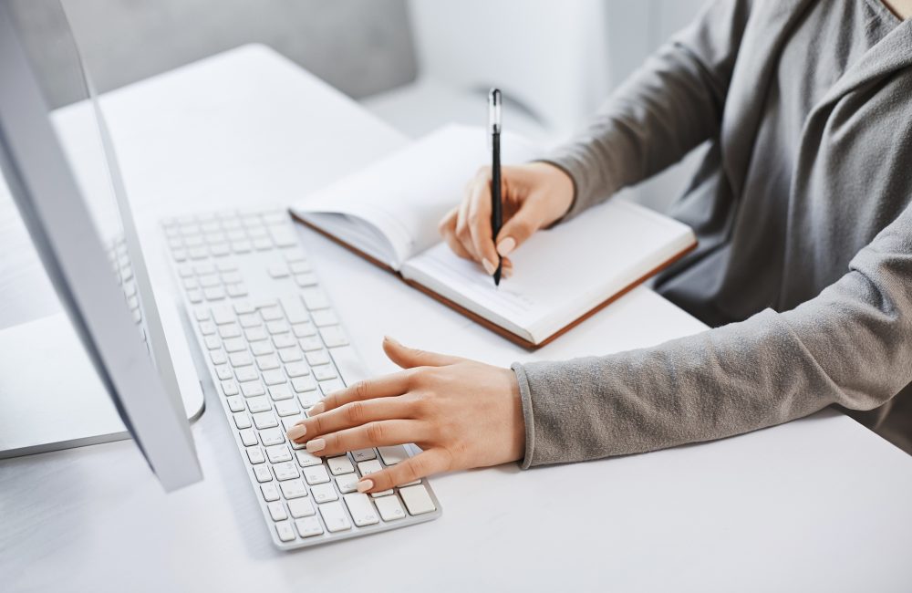 I can handle multi tasks. Cropped shot successful girl typing on keyboard and making notes while looking at computer screen and studying new business graphic. There is no time for rest.