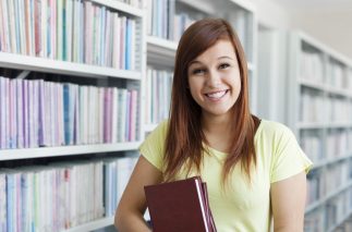 Cheerful student girl holding books in library